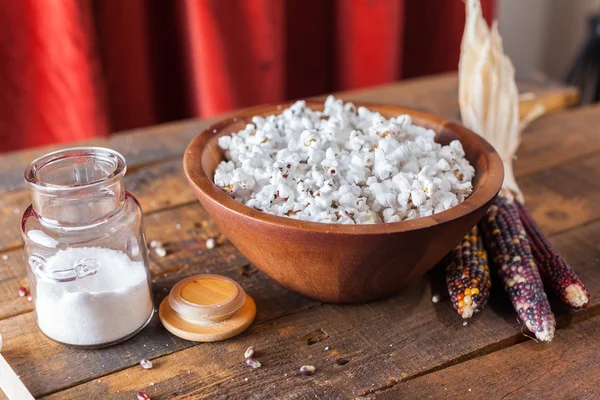 Frisch geknalltes Popcorn in Holzschale mit Körnern und Maiskolben auf dem Tisch — Stockfoto