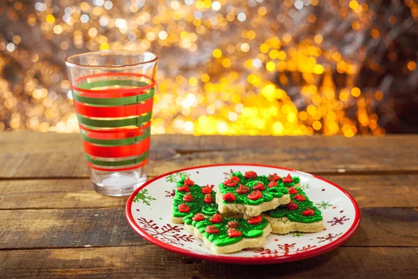 Galletas del árbol de Navidad en la placa de vacaciones con la taza de leche vacía por el fuego . —  Fotos de Stock