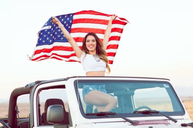 Mutlu genç kız Cabrio araba Amerikan bayrağı sallayarak Holding ayakta.