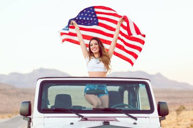 Mutlu genç kız Cabrio araba Amerikan bayrağı sallayarak Holding ayakta.