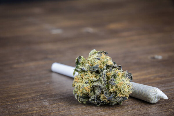 Macro Close Up Of Marijuana Bud With Joint On Wooden Table. Selective Focus With Copy Space.