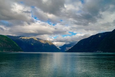Fiyort kıyısında bulutlu bir gökyüzü. Yeşil ormanlı dağlar, Eidfjord, Norveç