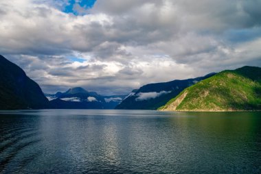 Fiyort kıyısında bulutlu bir gökyüzü. Yeşil ormanlı dağlar, Eidfjord, Norveç
