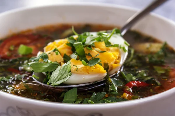 Spoon with chopped egg and greens lies on the surface of vegetable soup. Closeup — Stock Photo, Image