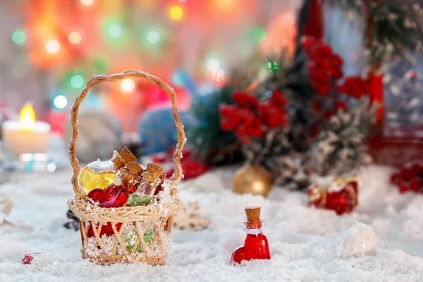 Kleine multi-gekleurde glazen flessen van Santa in een rieten mand met giften op de achtergrond van een rode lantaarn en New Year's decoraties. Bokeh. — Stockfoto