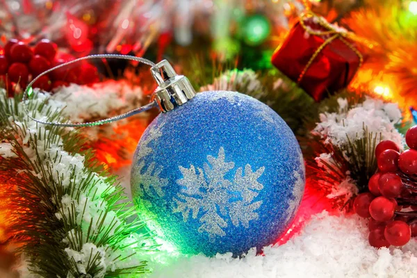 Ball on the snowy branches of a Christmas tree against a background of shiny tinsel. glowing lights. bokeh Stock Picture