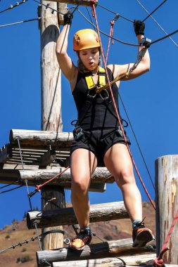 Macera tırmanma halat Parkı - koruyucu giysiler içinde genç bir kadın üzerinde bir ip simülatörü parça geçer. Eğitim dağcıların dağlarda