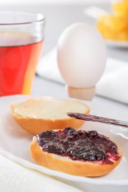 Haşlanmış yumurta, Fransız topuz, reçel, çay ve tereyağı kahvaltı. Bıçak reçel smear. Aydınlatmalar ışık