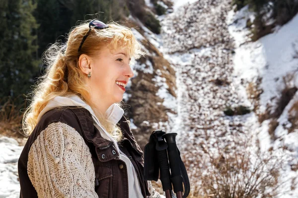 woman with walking sticks on a background of snow-capped mountains and forests in a bright sunny day