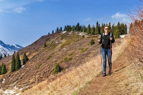 young girl with trekking sticks walks along the mountain trail