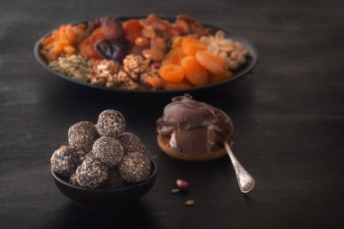 Doğal sağlıklı çiğ enerji ısırıkları, çikolata ezmesi ve kurutulmuş meyvelerin karışımı ve siyah bir masada fındık. Dikkat çekmeden. Boşluğu kopyala