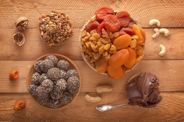 Natural healthy raw energy bites, chocolate paste and mix of dried fruits with nuts on a wooden table. Top view