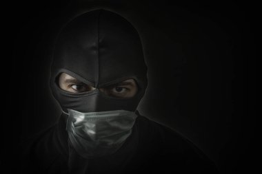 Siyah maskeli bir haydut. Gözlerinde delik ve tıbbi maske var. Alçak kapak. Yakın plan. Boşluğu kopyala