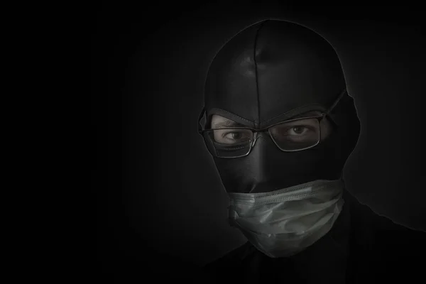 Bandit in a black mask with a slit for the eyes, glasses and a medical mask. Low hatch. Close-up. Copy space