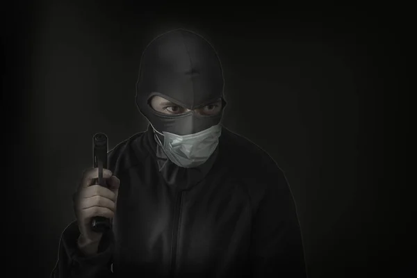 Bandit in a black mask with a slot for the eyes and a medical mask with a gun in his hands. Low hatch. Close-up. Copy space