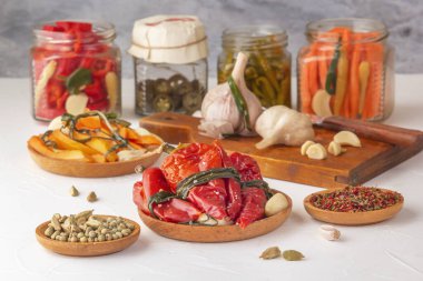 Hafif ahşap bir masanın üzerindeki baharatlarla bağışıklığı artırmak için mayalanmış kırmızı biberler ve turşulu cam kavanozlar.