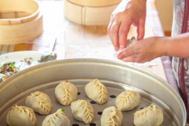 Kadın elleri manti, khinkali, hamur köftesi veya hamur işlerinden kıymalı et doldurma ve mutfak masasının arka planında çift katlı kazan ile yeşillikler yapar. Ev yapımı yemek..