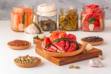 Hafif ahşap bir masanın üzerindeki baharatlarla bağışıklığı artırmak için mayalanmış kırmızı biberler ve turşulu cam kavanozlar.