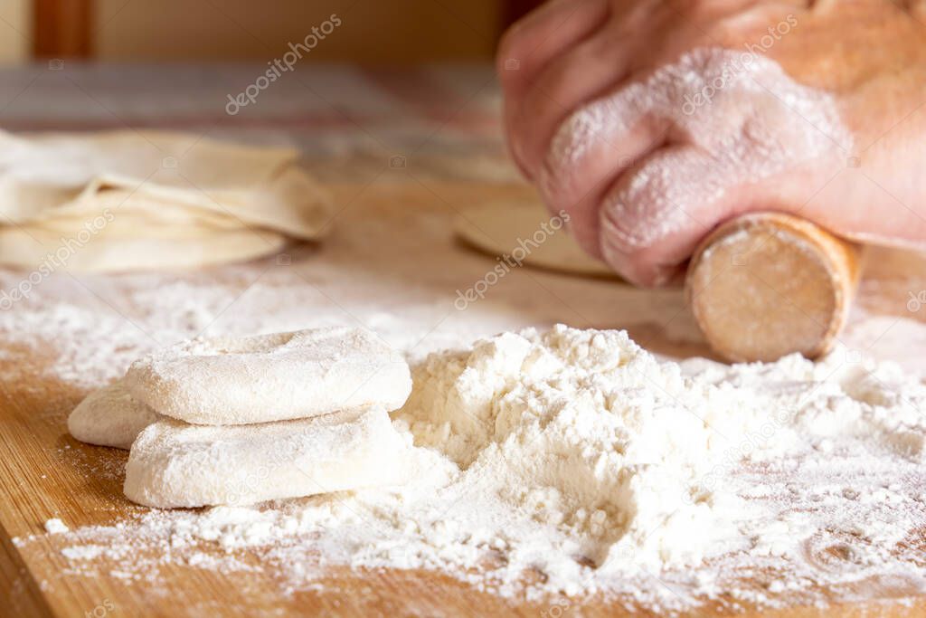 Female hands roll out the dough with a wooden rolling pin on a board with flour. Close-up