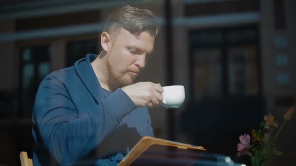 El joven toma café y lee noticias en la tableta — Vídeos de Stock