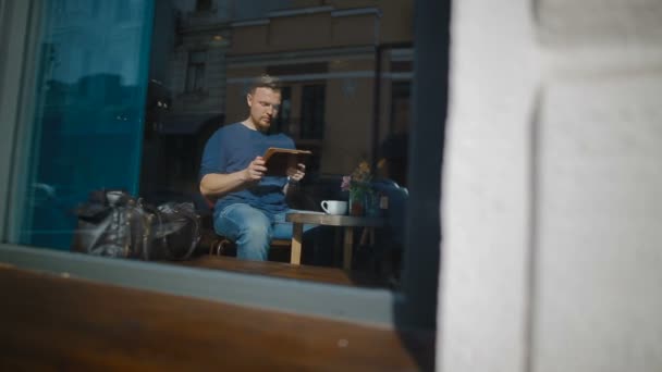 O homem trabalha no tablet sentado na cafetaria — Vídeo de Stock