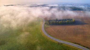 Kısmen Sis tarafından kapalı eğri hız yolda havadan görünümü. Eğri yol kahverengi ve yeşil yarım yatay bölme. Sonbahar, sisli sabah kırsal kırsalında dikey görünüm. Puslu çek manzara.  
