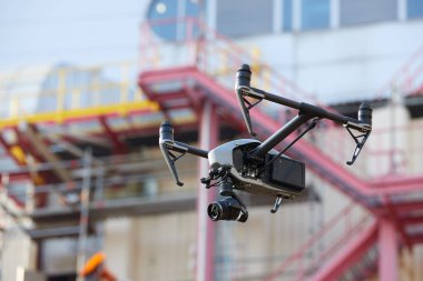 Visual inspection in industry. Controlling of hard to reach objects from the air in the industry. Side view. Hovering  black quadcopter with  powerful camera against blurred industrial construction.