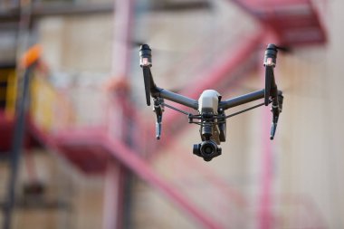 Visual inspection in industry. Controlling of hard to reach objects from the air in the industry. Side view. Hovering  black quadcopter with  powerful camera against blurred industrial construction.