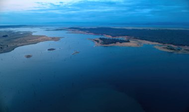 Akşamüstü, batan güneşle birlikte Afrika Gölü Kariba 'nın ve çevresindeki manzaranın havadan görüntüsü. Mavi ve pembe renkler. Sudaki ölü ağaçlar. Zimbabwe. Safari Kariba Gölü kıyısında kamp yapıyor..