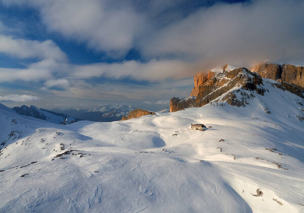 Aerial, panoramic winter view on beautiful touristic mountain hut. Dolomites mountainscape from above.  Pale di San Martino mountains range, covered in snow.  Rosetta, San Martino di Castrozza, Italy.