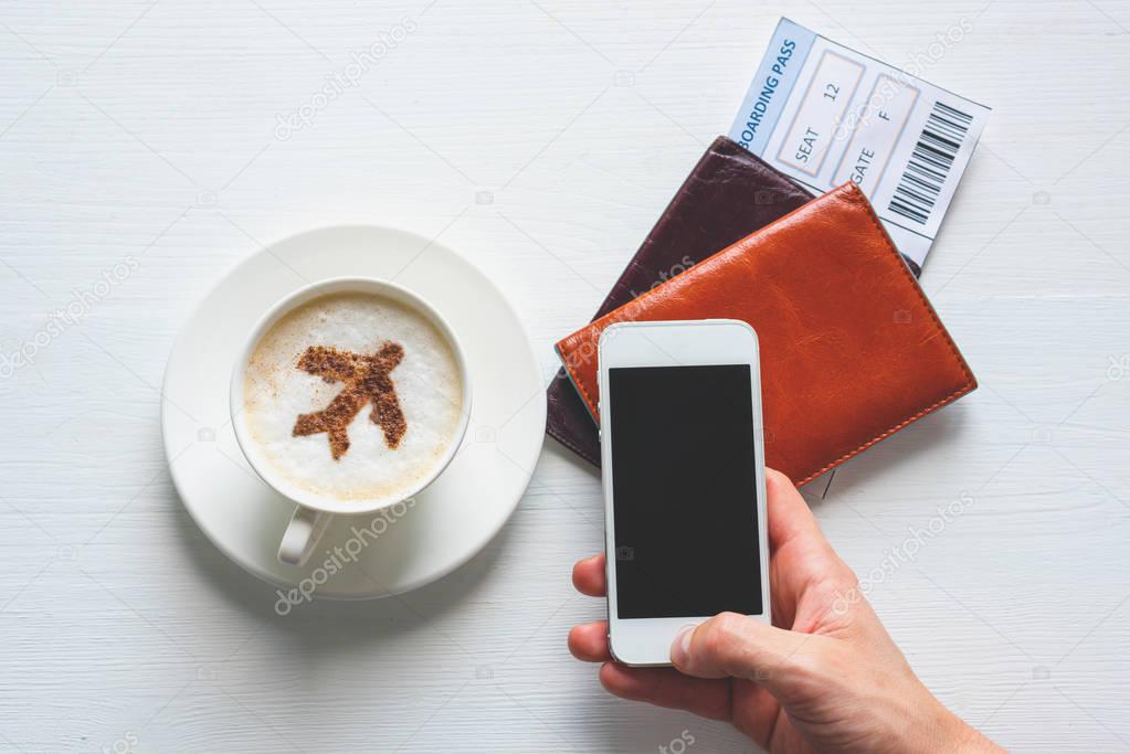 Cup of coffee with aircraft made of cinnamon powder, passports,boarding passes and smartphone screen