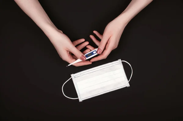 Kadın elleri termometre ve yüz maskesi ile