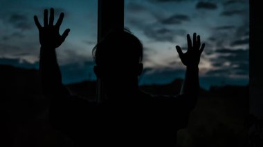 Gün batımında pencereden dışarı bakan bir adam ve dairede üzgün bir adam. Genç bir adamın hayat tarzı görüntüsü.