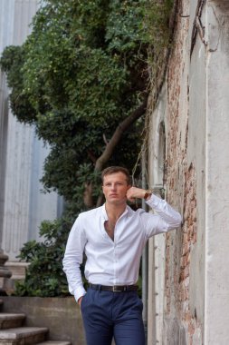 Beyaz gömlekli yakışıklı ve genç adam Venedik 'te bir duvara yaslanmış yaz havasının tadını çıkarıyor..