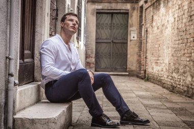 Genç adam beyaz gömlekli ve klasik siyah ayakkabılı basamaklarda oturuyor..