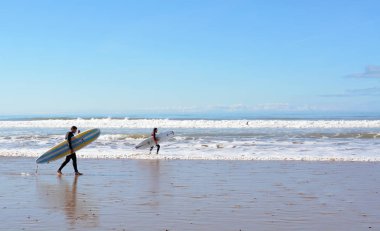 Sidi Kaouki, Fas - 7 Ocak 2016: Essaouira yakınındaki plajda sörf tahtası taşıyan iki sörfçü