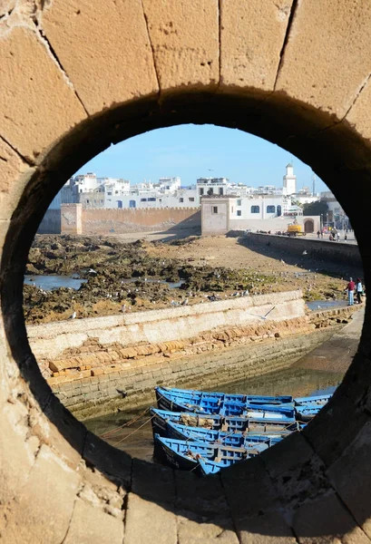 Essaouira, Maroko - 5 stycznia 2016: Okrągłe okno w fortyfikacji historycznego portu i niebieski łodzi — Zdjęcie stockowe