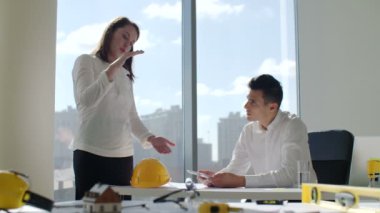 Mimarlar tarafından beyaz modern ofis İnşaat şirketi büyük panoramik pencerenin önünde tabloda oturur. şehir manzarası arka plan. Bina inşaat proje üzerinde çalıştıklarını