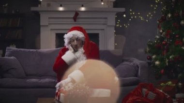 Genç adam kostüm Noel Baba mobile tarafından arka planda Noel ağacı konuşuyor