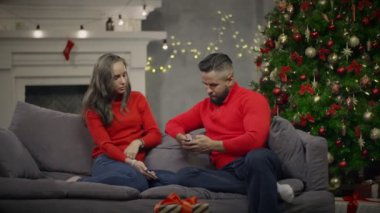 Kanepe ve hareket eden kullanma ve arka plan üzerinde Noel ağacı konuşuyor genç Çift