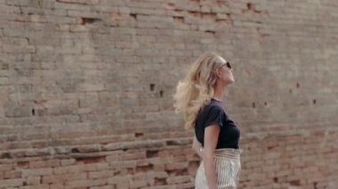 Tuğla arka planda şehir sokak üzerinde yürüyen güneş gözlüklü seksi sarışın kadın