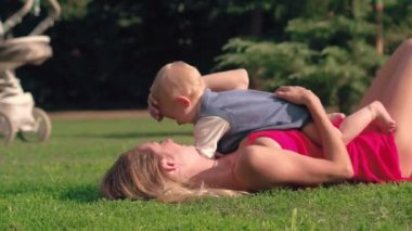 Mutlu anne ve bebek çayır, yeşil çimenlerin üzerinde park güneşli bir günde yalan