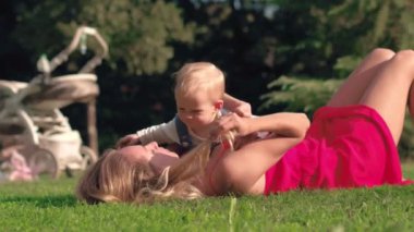 Genç anne ve bebek çayır yaz Park, yeşil çim üzerinde yalan