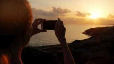 Genç kadın fotoğraf yapma telefon güzel günbatımı deniz. Deniz manzara günbatımı