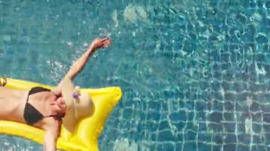 Şapka ve sarı şişme yüzme havuzunda yüzen mayolu rahatlatıcı kadın
