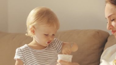 Komik çocuk genç anne yanındaki koltukta oturan yoğurt yeme