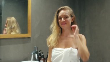 Kadın için sarı saç tarak kullanarak ve kameraya bakarak beyaz banyo havlusu