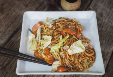 Yakisoba sosis Japon usulü kızarmış şehriye ile beyaz tabakta tatlı soslu ve düşük güneş ışığıyla.