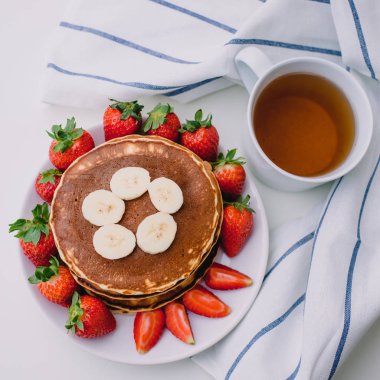 Sağlıklı kahvaltı. Krep çilek, muz, beyaz havlu ile beyaz arka planda siyah çay