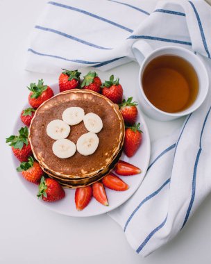 Sağlıklı kahvaltı. Krep çilek, muz, beyaz havlu ile beyaz arka planda siyah çay
